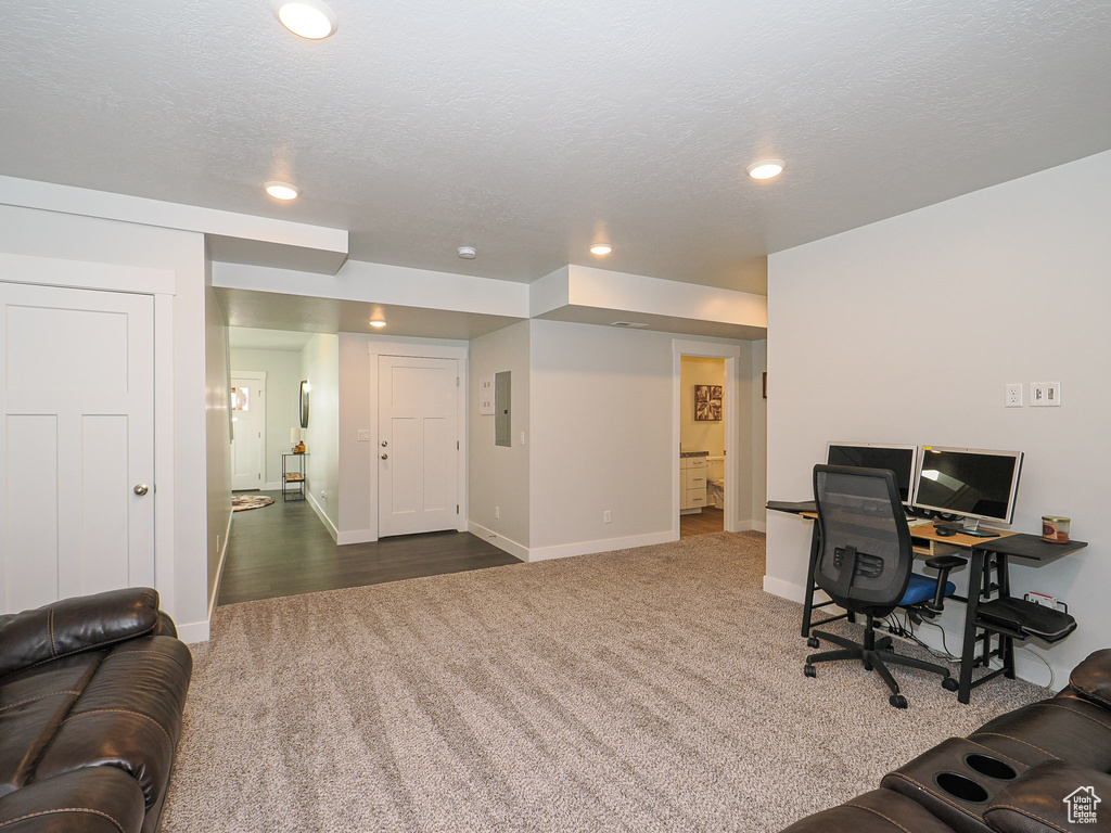 Office area with dark colored carpet, electric panel, and a textured ceiling