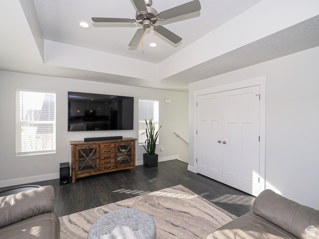 Living room with dark hardwood / wood-style flooring, ceiling fan, a raised ceiling, and a healthy amount of sunlight