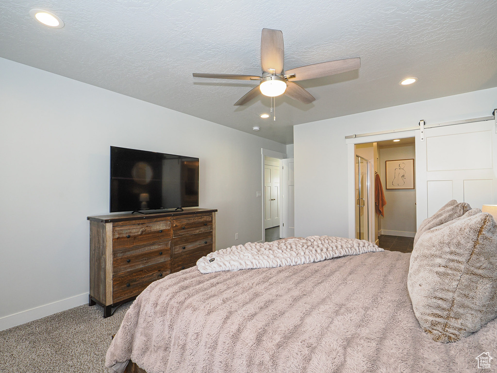 Bedroom with ceiling fan, a barn door, a textured ceiling, and carpet flooring