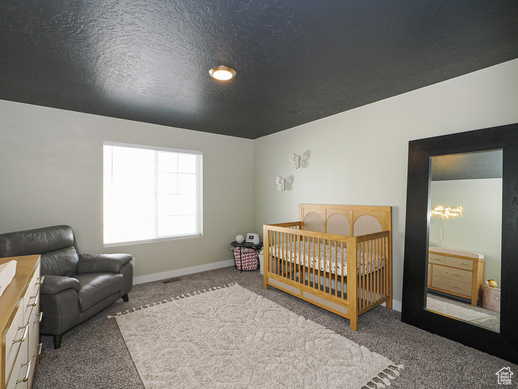 Bedroom with a crib, carpet floors, and a textured ceiling