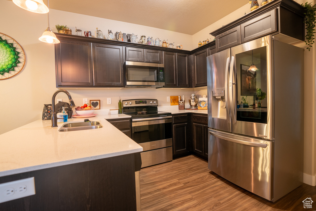 Kitchen with sink, appliances with stainless steel finishes, hanging light fixtures, dark brown cabinetry, and light hardwood / wood-style floors