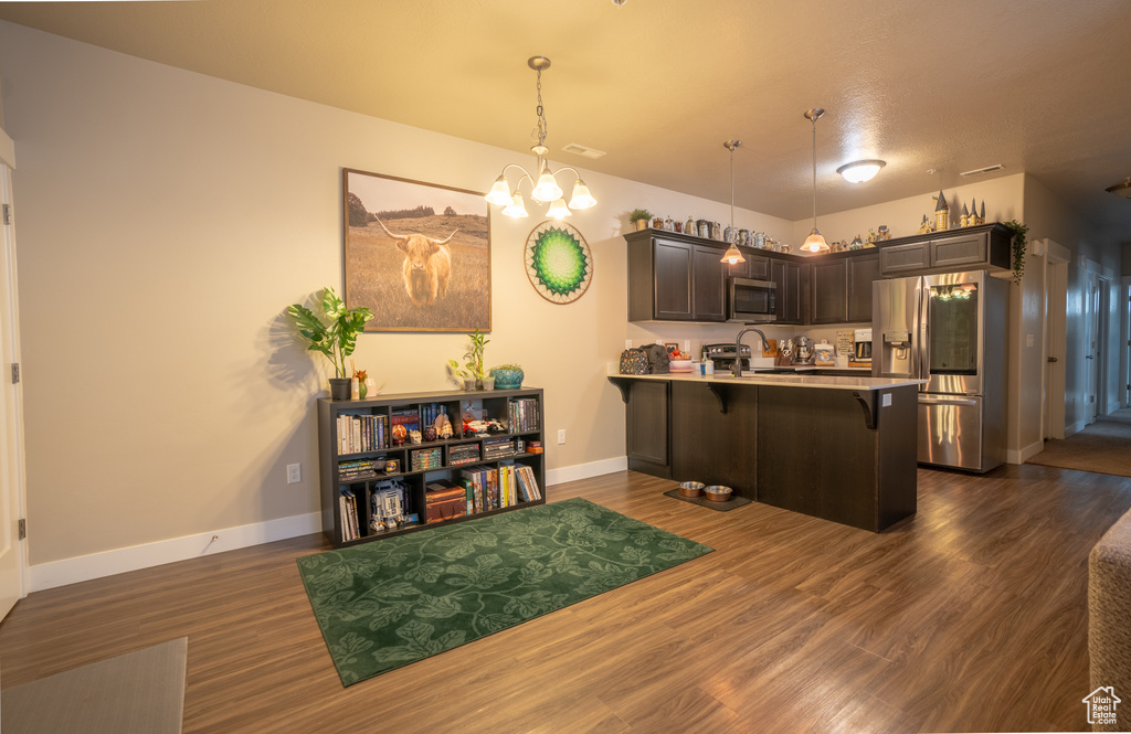 Kitchen featuring decorative light fixtures, dark brown cabinets, appliances with stainless steel finishes, a kitchen breakfast bar, and kitchen peninsula