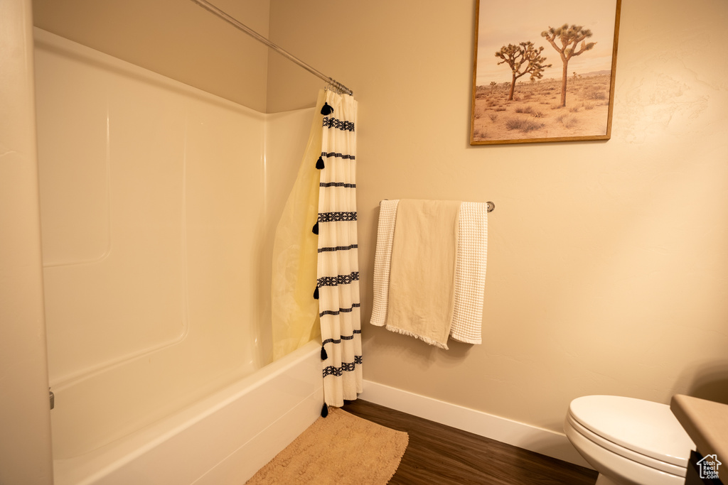 Bathroom featuring hardwood / wood-style floors, shower / bath combination with curtain, and toilet