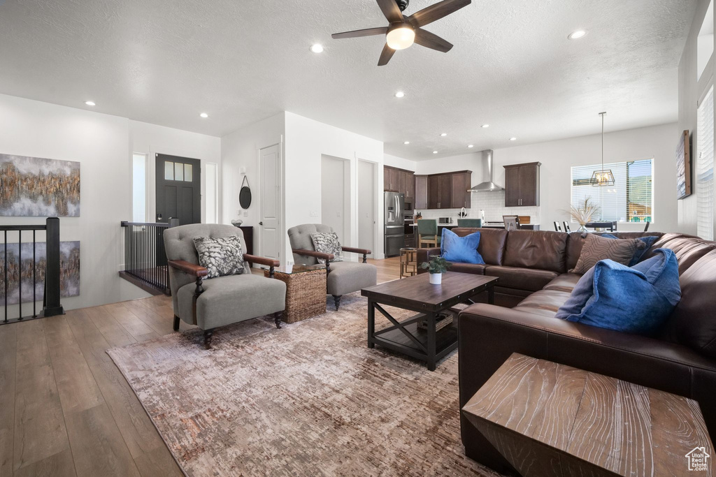 Living room with ceiling fan, a textured ceiling, and light wood-type flooring