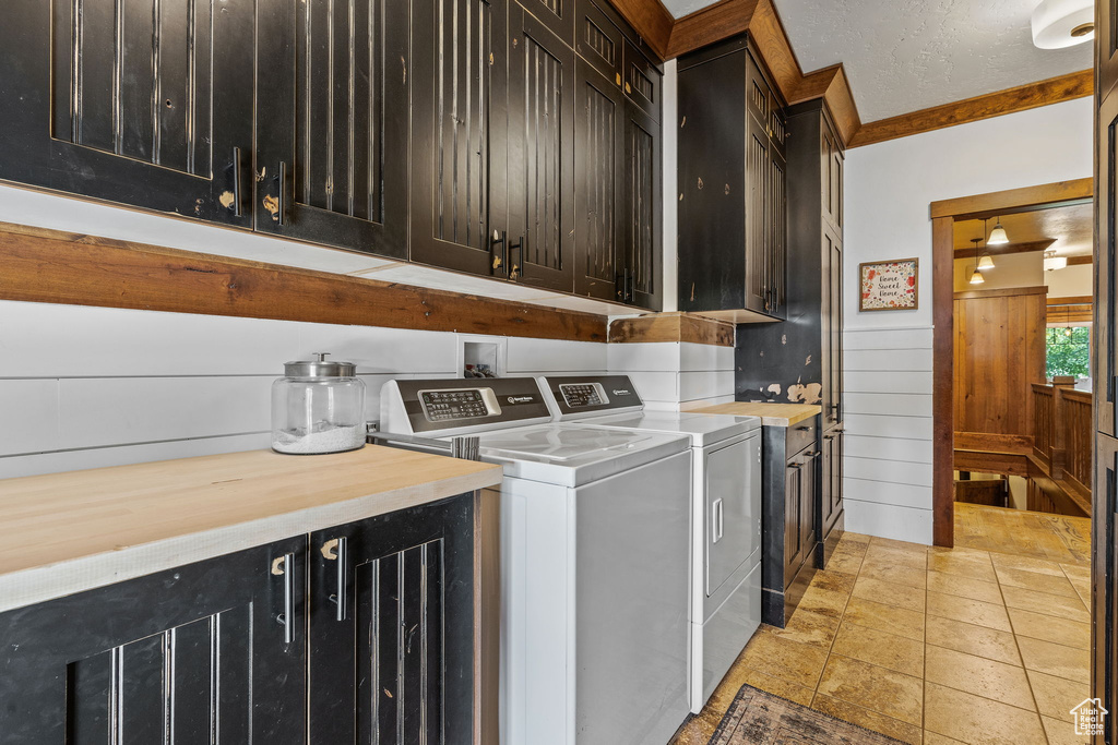 Washroom featuring washing machine and clothes dryer, cabinets, a textured ceiling, ornamental molding, and wooden walls