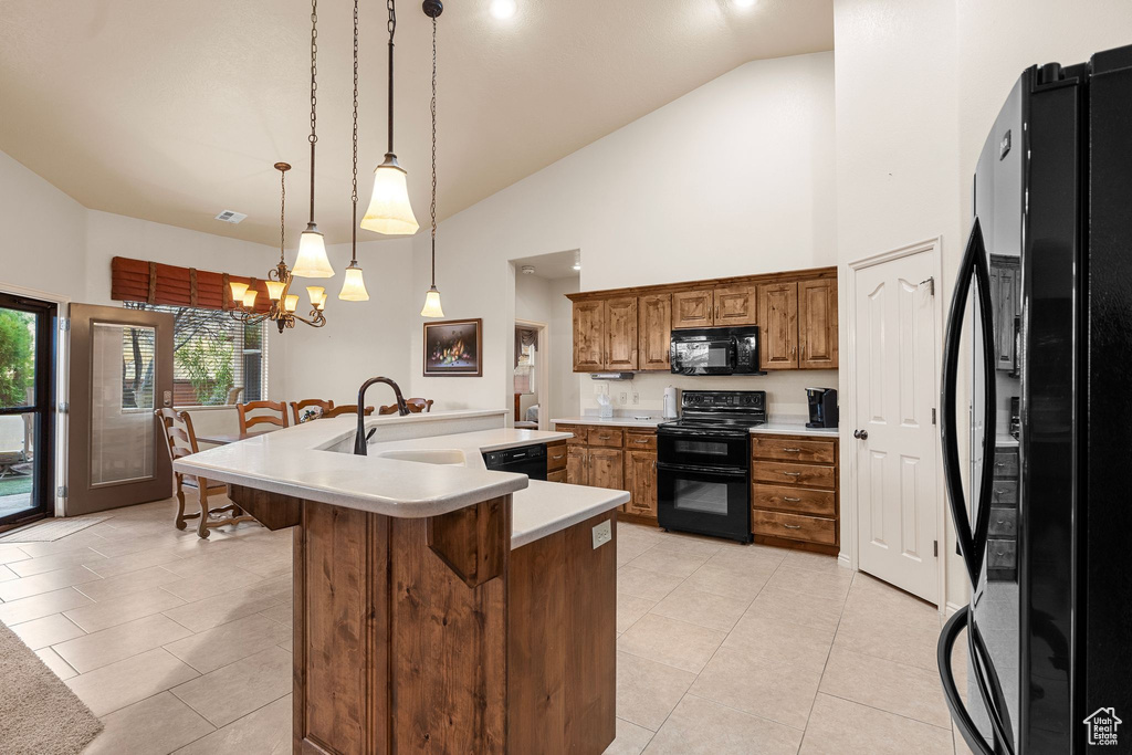 Kitchen with a breakfast bar, sink, hanging light fixtures, black appliances, and a center island with sink