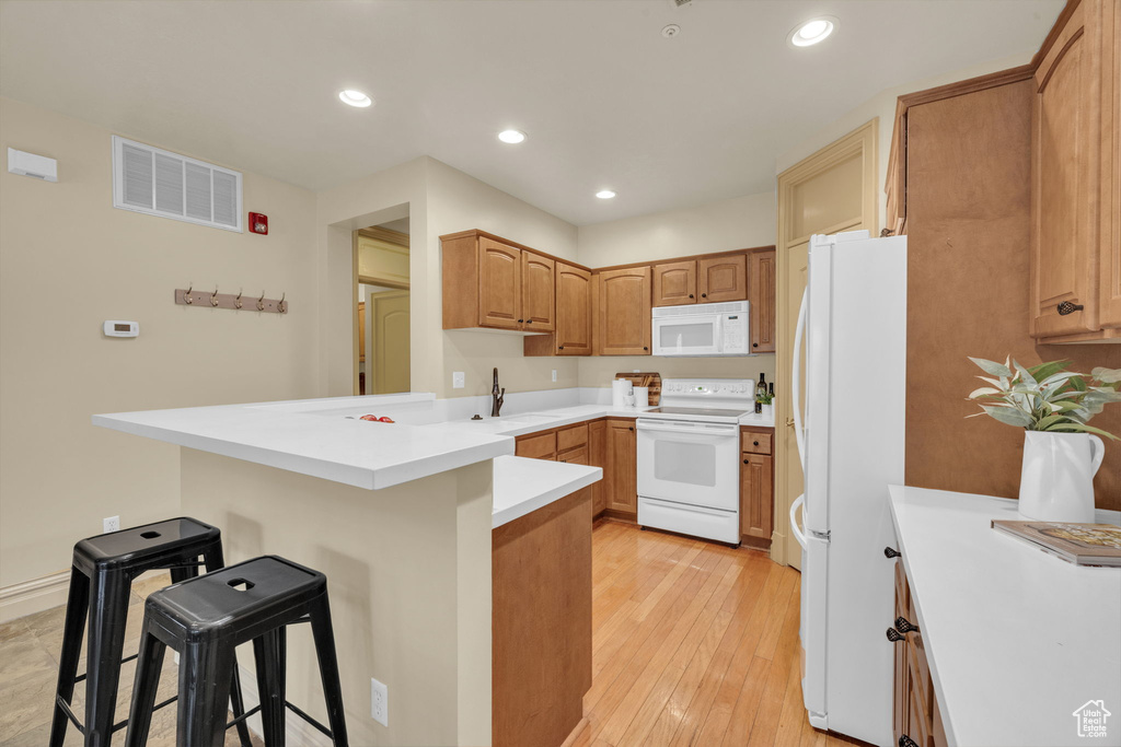 Kitchen with a kitchen bar, sink, light hardwood / wood-style flooring, kitchen peninsula, and white appliances
