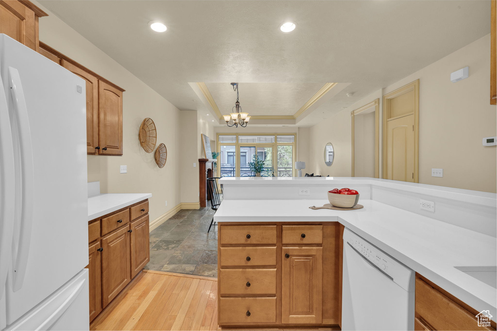 Kitchen featuring pendant lighting, a notable chandelier, a raised ceiling, white appliances, and light hardwood / wood-style flooring