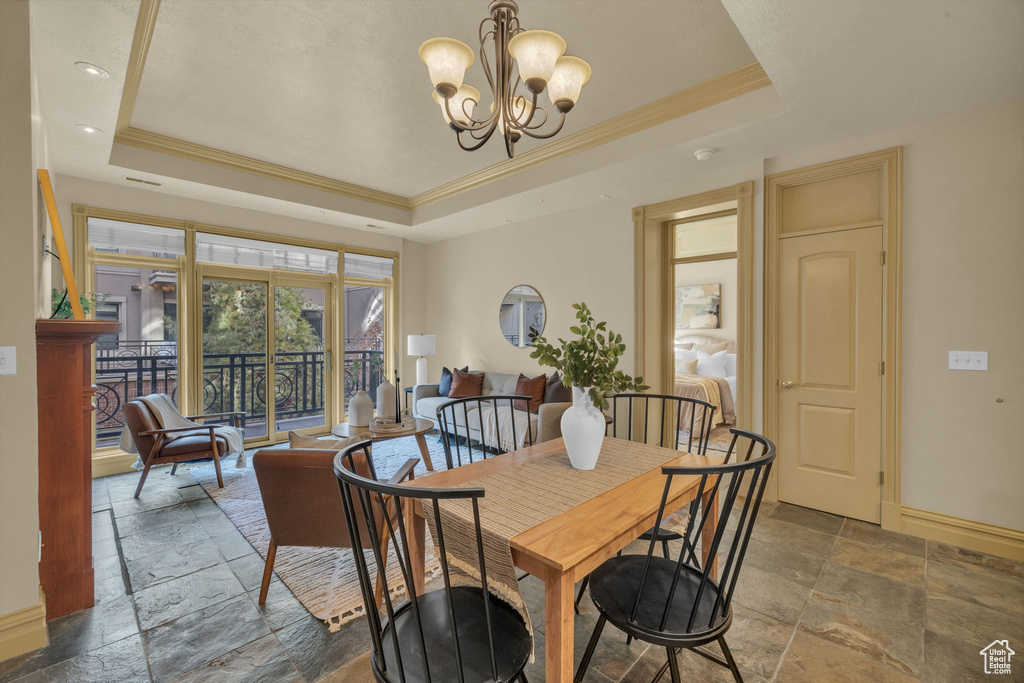 Dining space with an inviting chandelier, a tray ceiling, and ornamental molding