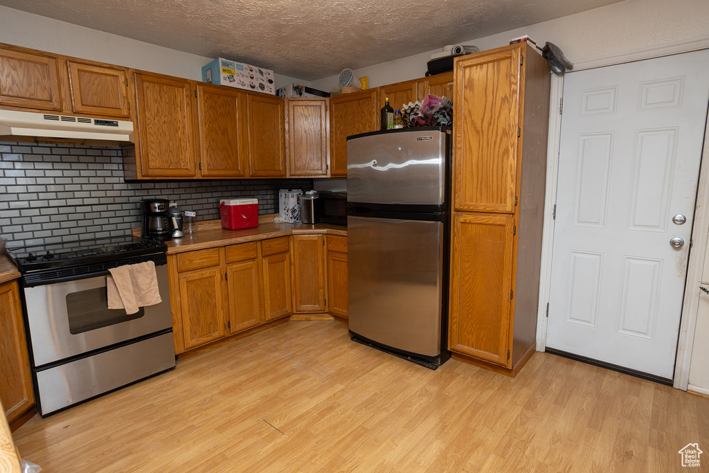 Kitchen with stainless steel appliances, backsplash, a textured ceiling, and light hardwood / wood-style flooring