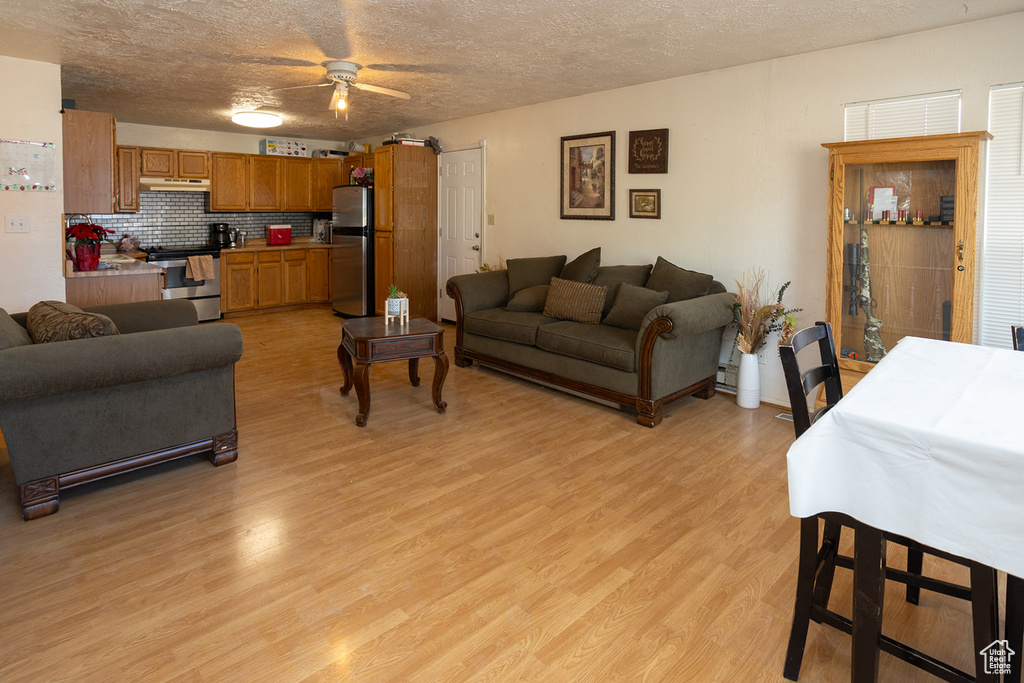 Living room with ceiling fan, a textured ceiling, and light wood-type flooring