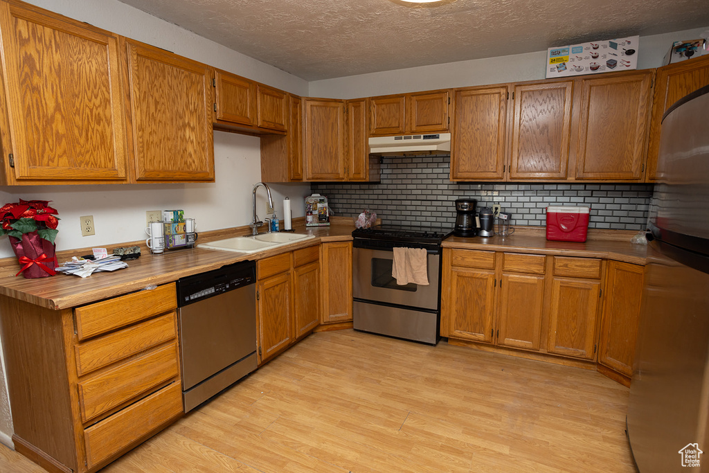 Kitchen with appliances with stainless steel finishes, sink, light wood-type flooring, and decorative backsplash