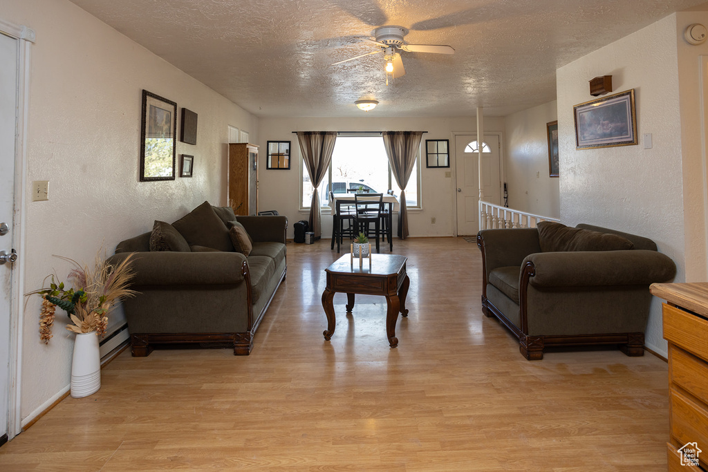 Living room with ceiling fan, a textured ceiling, and light wood-type flooring