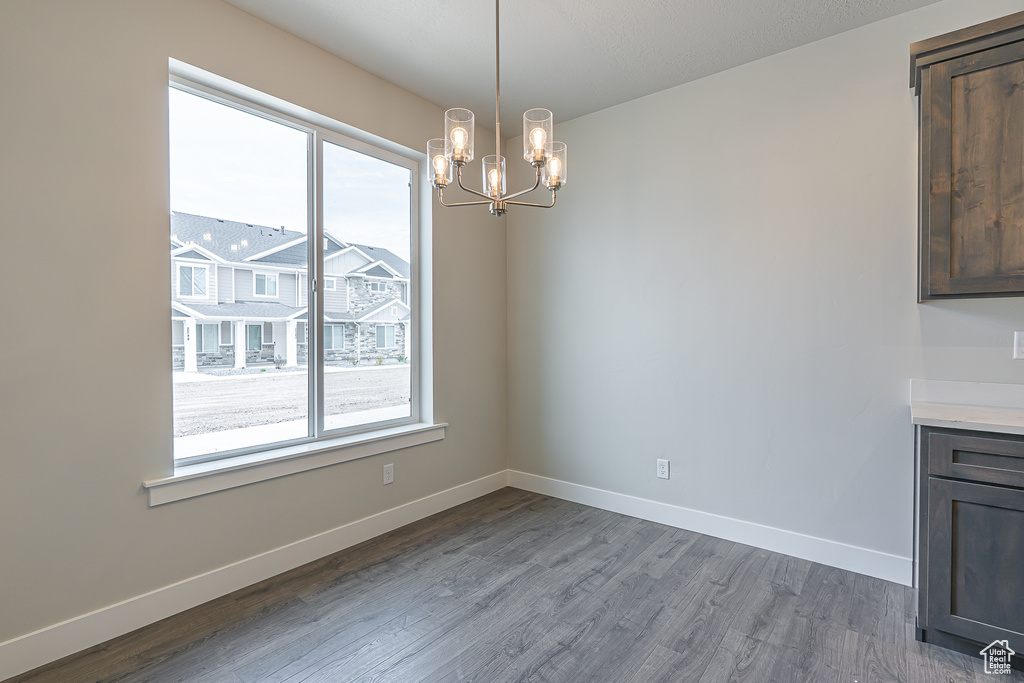 Unfurnished dining area with baseboards, wood finished floors, and a notable chandelier