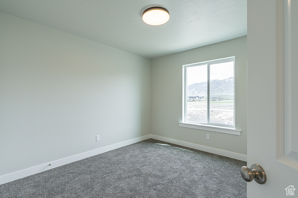 Unfurnished room with baseboards, a mountain view, and dark carpet
