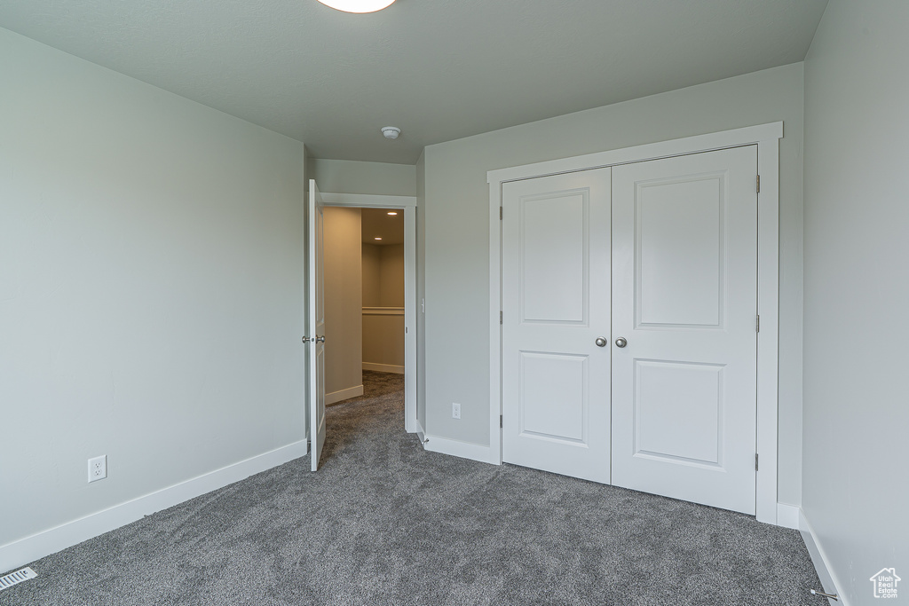 Unfurnished bedroom featuring dark colored carpet, baseboards, and a closet