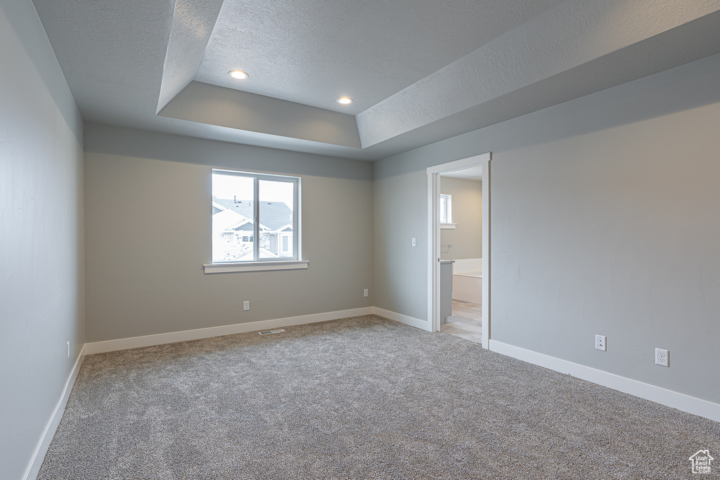 Spare room featuring light carpet, a raised ceiling, a textured ceiling, recessed lighting, and baseboards