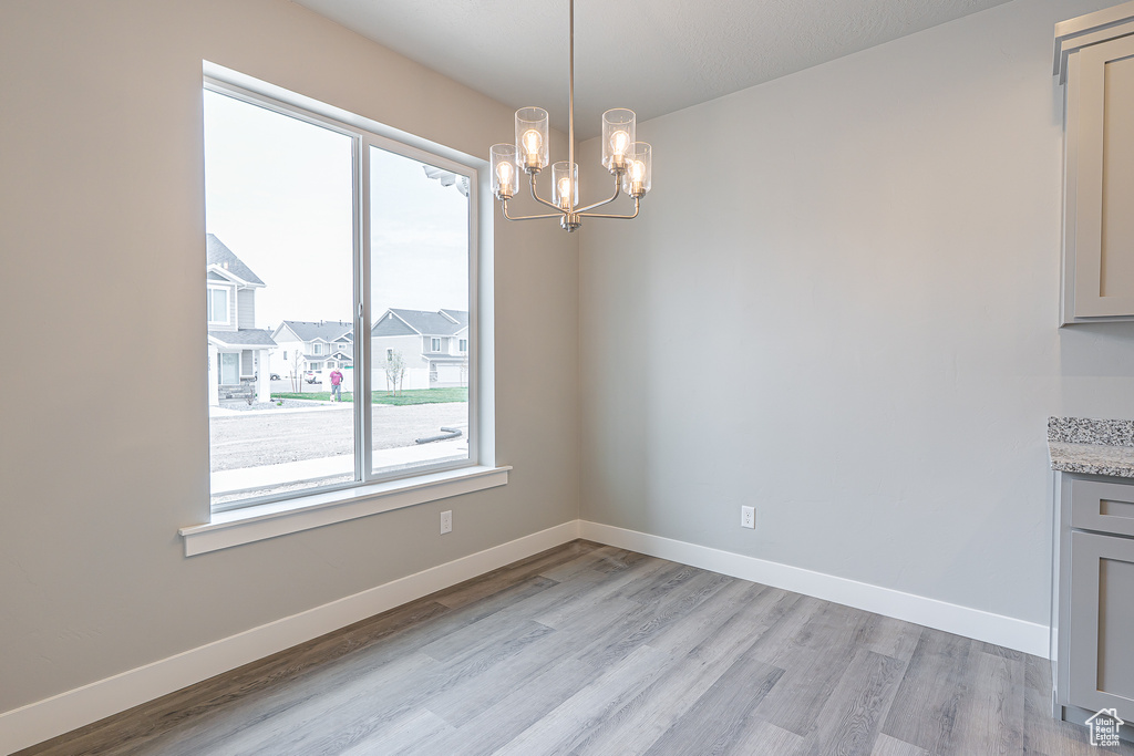 Unfurnished dining area featuring baseboards, an inviting chandelier, plenty of natural light, and light wood finished floors