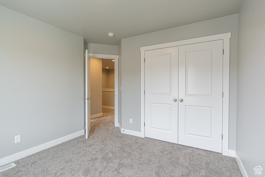 Unfurnished bedroom with visible vents, carpet, and a closet