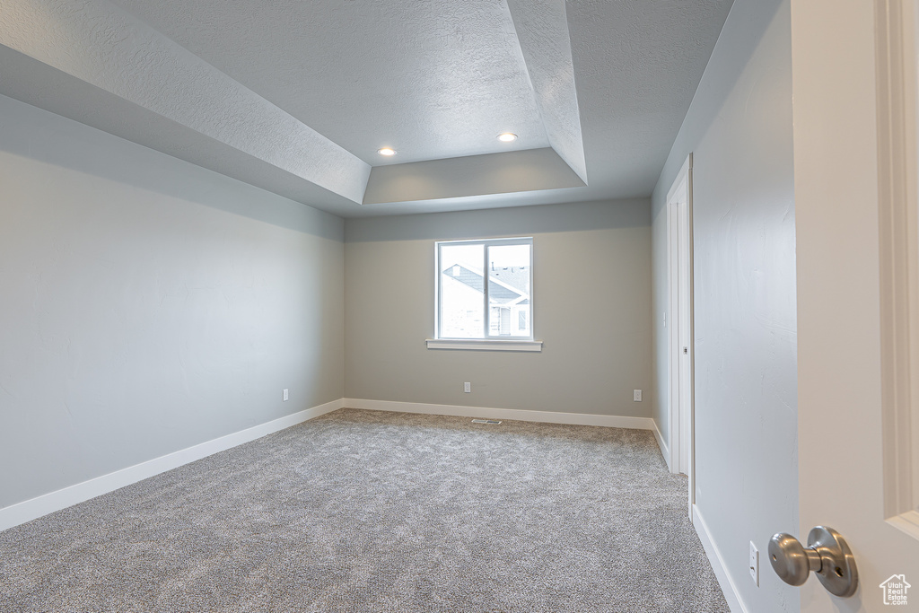 Unfurnished room featuring a textured ceiling, a raised ceiling, baseboards, carpet, and recessed lighting