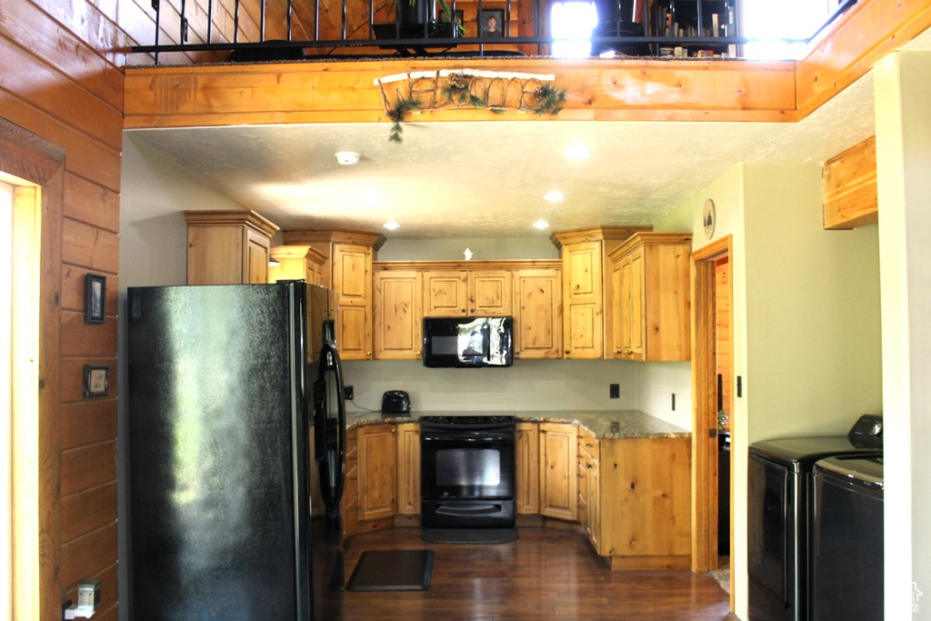 Kitchen with black appliances, separate washer and dryer, dark wood-type flooring, and light stone countertops