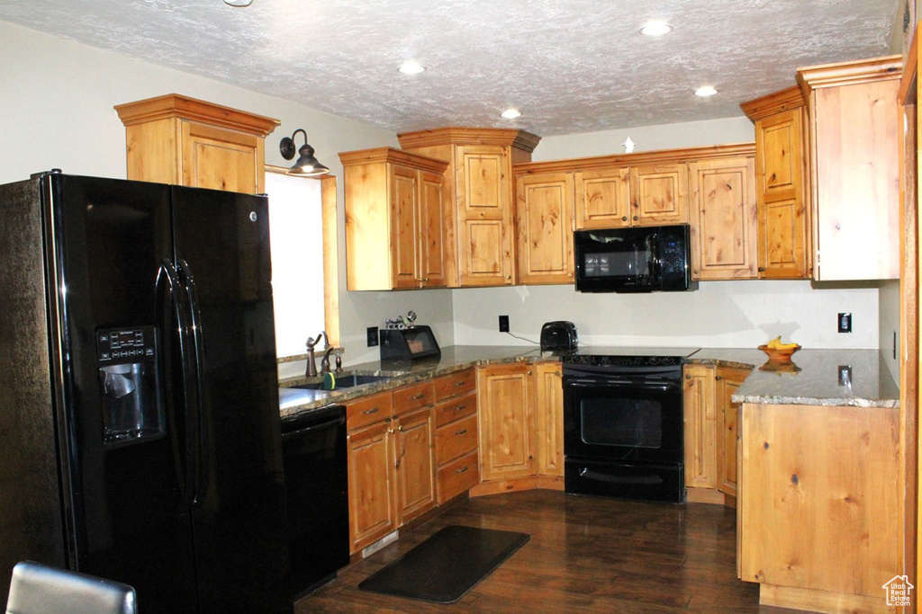 Kitchen featuring sink, dark hardwood / wood-style flooring, black appliances, light stone countertops, and a textured ceiling