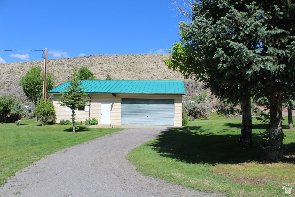 View of front of property with dirt driveway, a garage, a front yard, and metal roof
