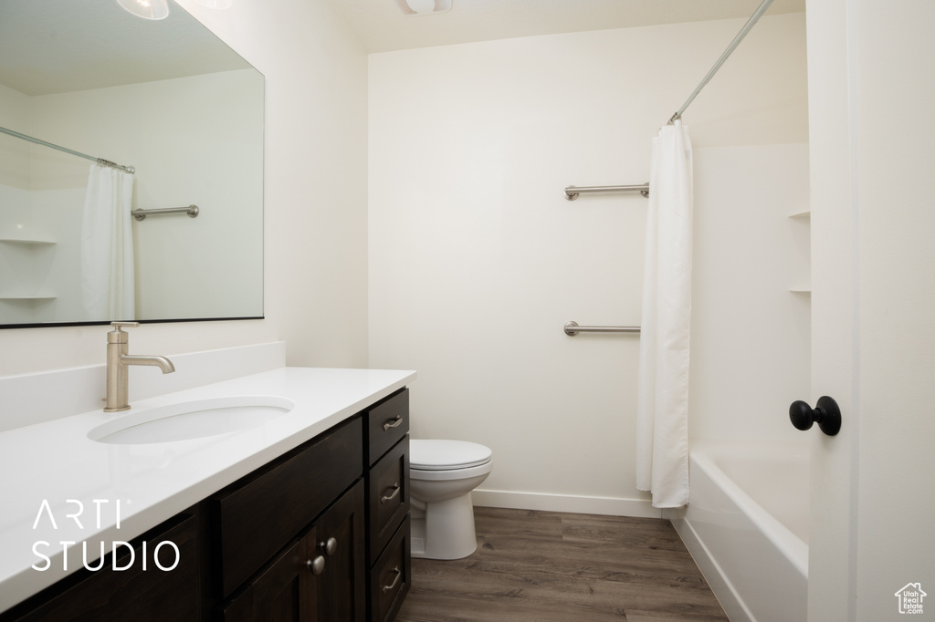 Full bathroom featuring shower / bathtub combination with curtain, vanity, toilet, and hardwood / wood-style floors