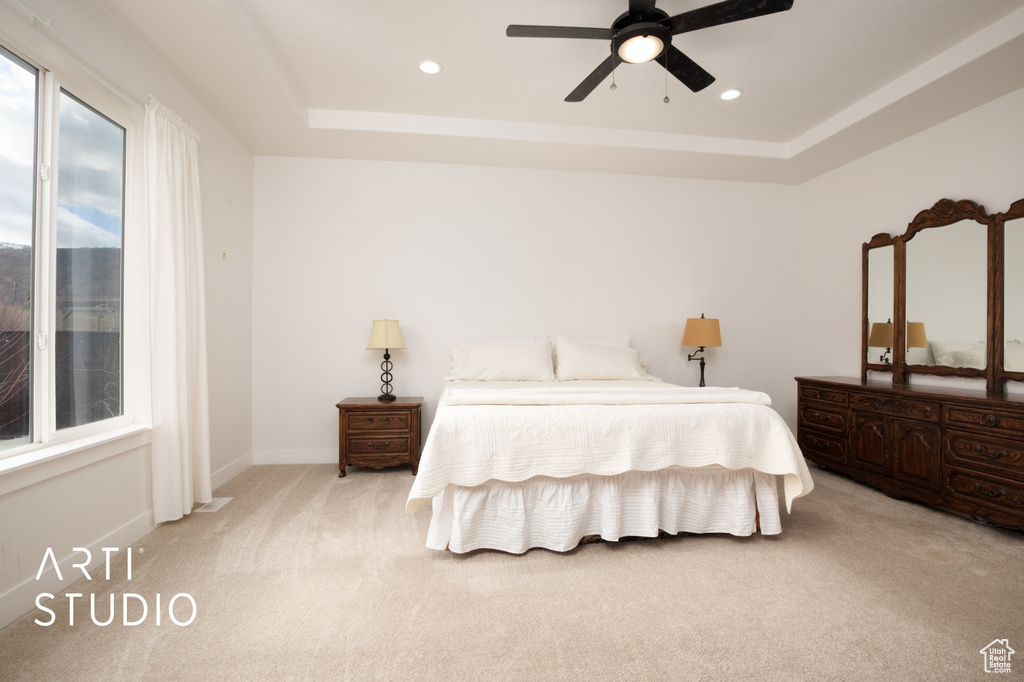 Carpeted bedroom featuring a raised ceiling and ceiling fan