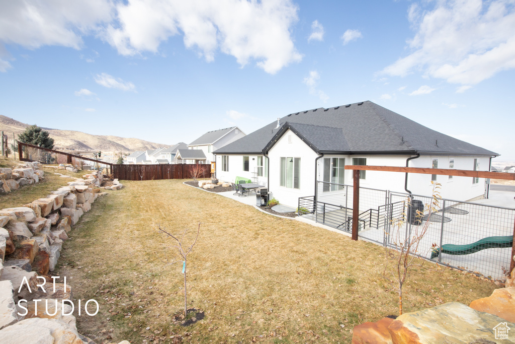 Rear view of property featuring a mountain view, a patio, and a lawn