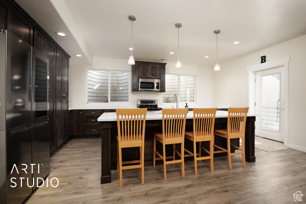 Kitchen featuring light hardwood / wood-style flooring, appliances with stainless steel finishes, hanging light fixtures, a center island, and a kitchen bar