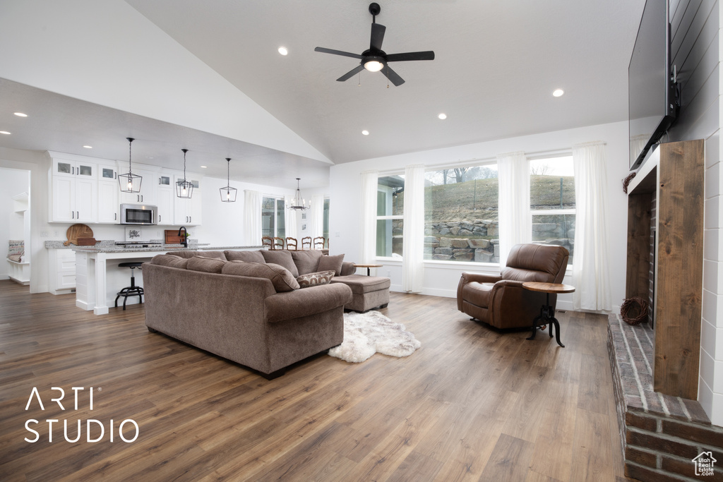 Living room featuring ceiling fan with notable chandelier, wood-type flooring, and high vaulted ceiling