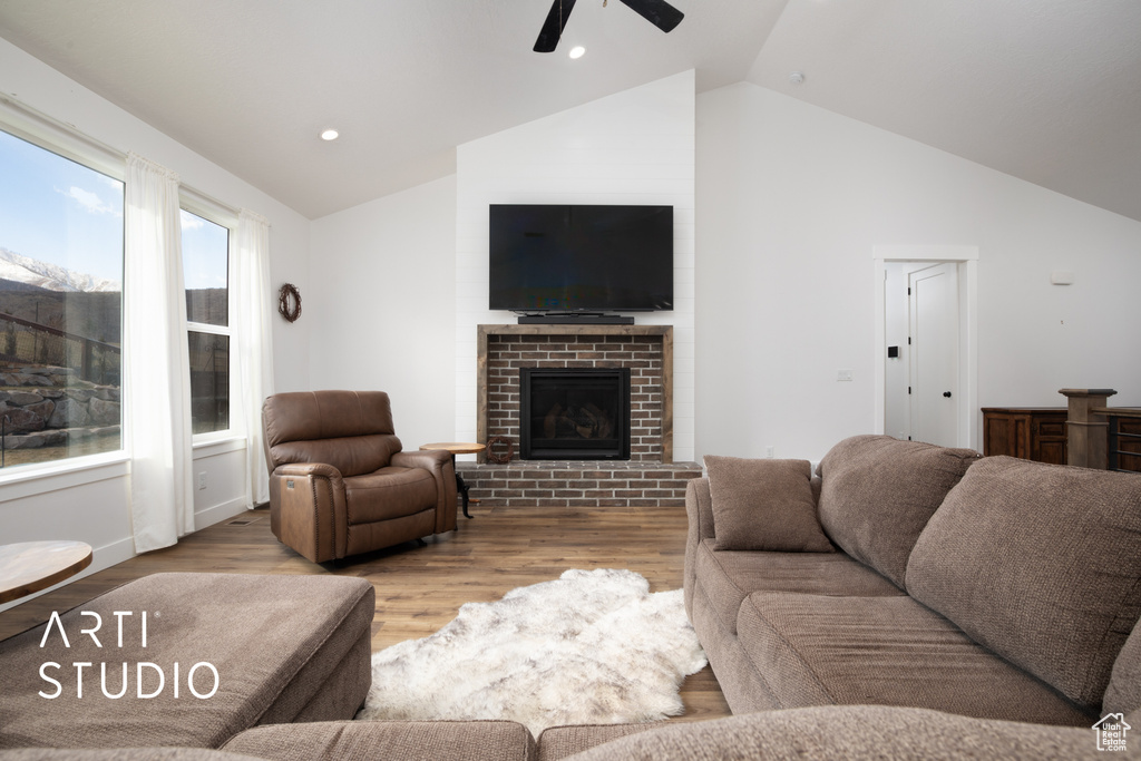 Living room featuring ceiling fan, high vaulted ceiling, light wood-type flooring, and a fireplace