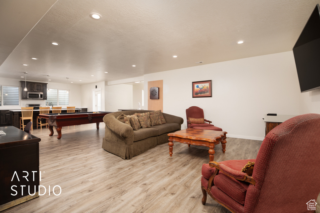Living room featuring pool table, a textured ceiling, and light wood-type flooring