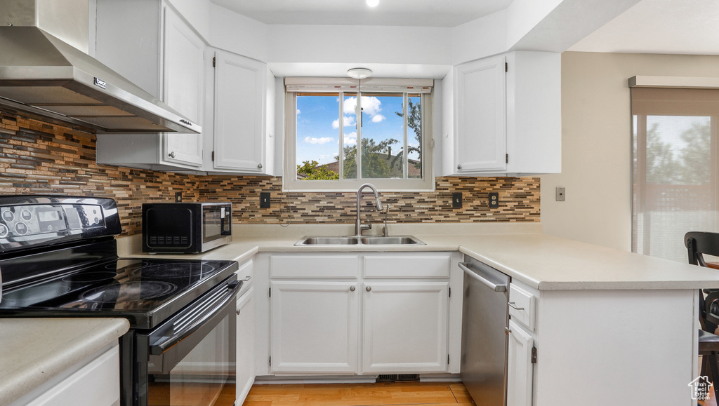 Kitchen featuring black appliances, wall chimney range hood, a peninsula, decorative backsplash, and white cabinets