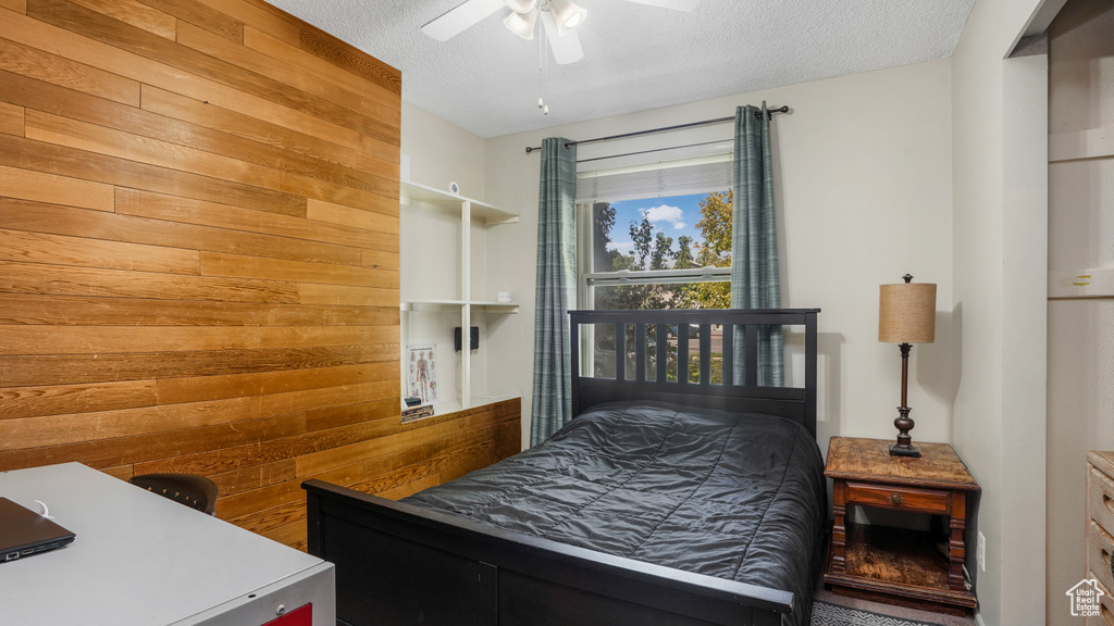 Bedroom featuring wood walls, a textured ceiling, and ceiling fan