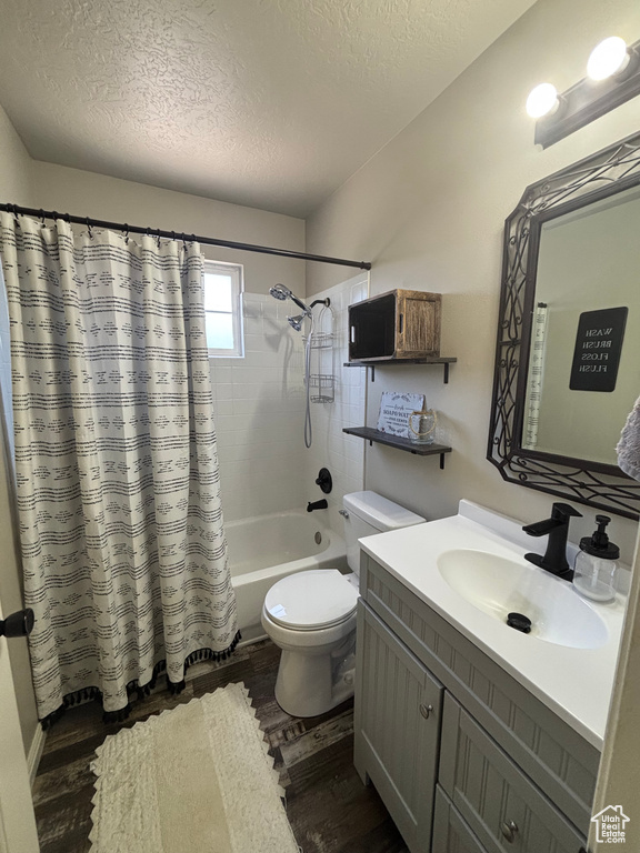 Bathroom with wood finished floors, a textured ceiling, vanity, shower / tub combo with curtain, and toilet