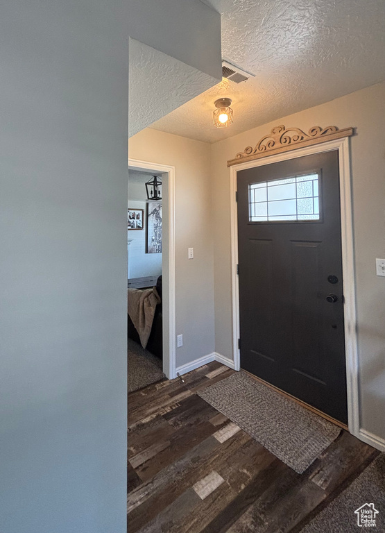 Foyer entrance featuring dark wood-type flooring, a textured ceiling, and baseboards