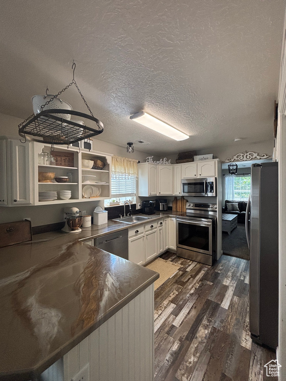 Kitchen with stainless steel appliances, a sink, plenty of natural light, white cabinetry, and a textured ceiling