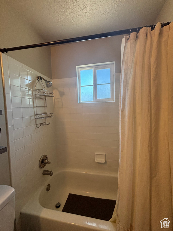 Full bathroom with shower / tub combo, toilet, and a textured ceiling