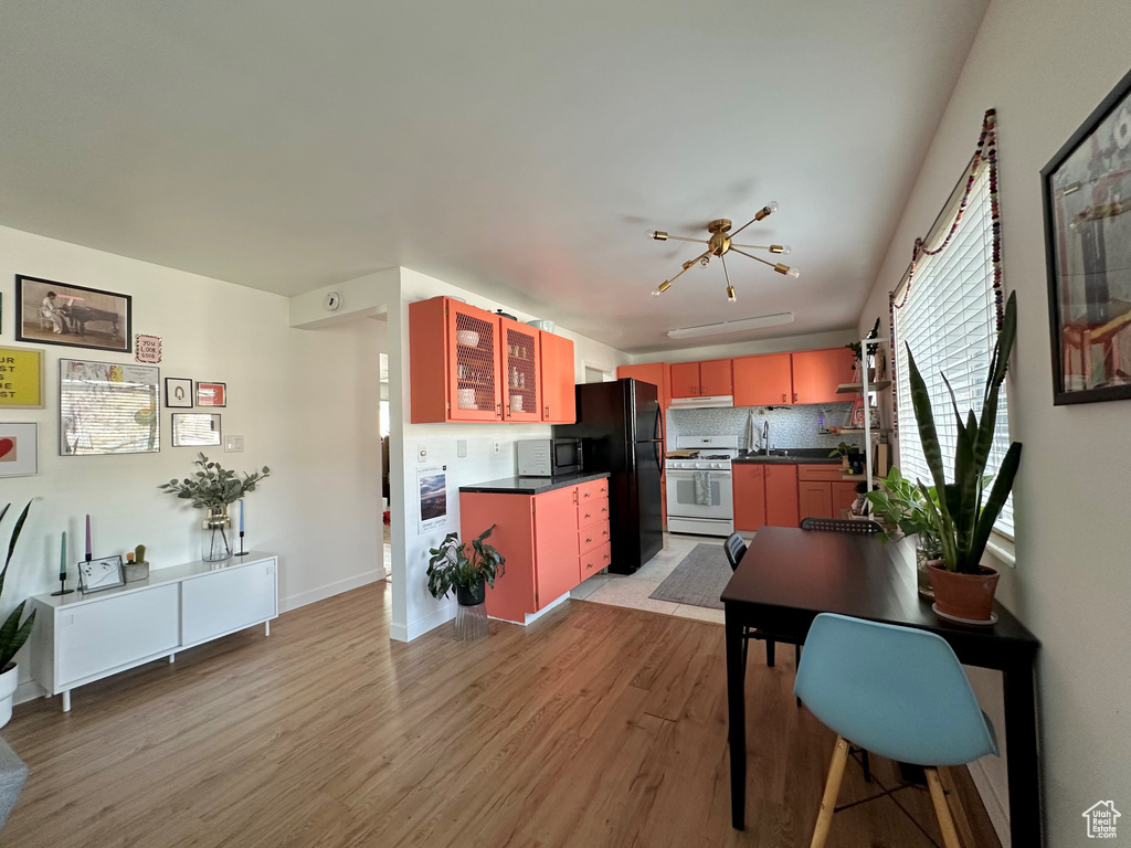 Kitchen with white range with gas cooktop, decorative backsplash, light hardwood / wood-style flooring, and black refrigerator