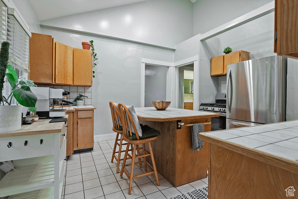 Kitchen featuring tile countertops, decorative backsplash, a center island, light tile patterned floors, and stainless steel appliances