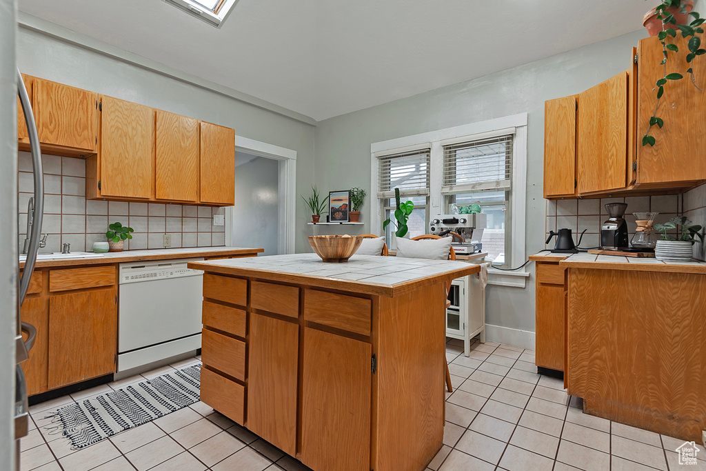 Kitchen with tasteful backsplash, tile countertops, a center island, light tile patterned floors, and white dishwasher