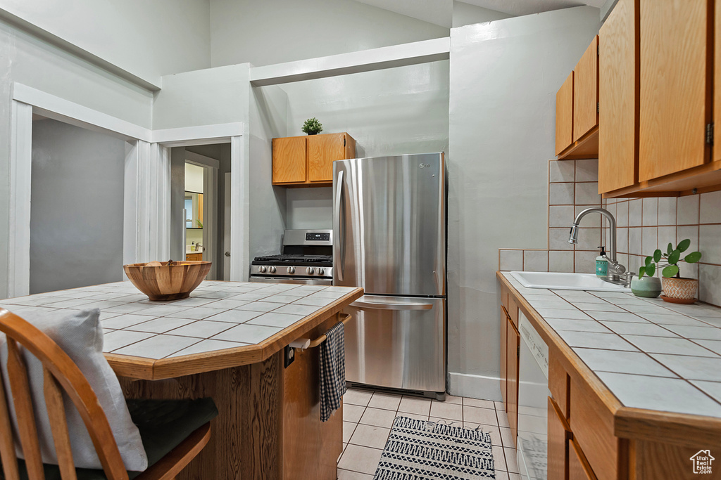 Kitchen featuring sink, decorative backsplash, tile counters, light tile patterned floors, and stainless steel appliances