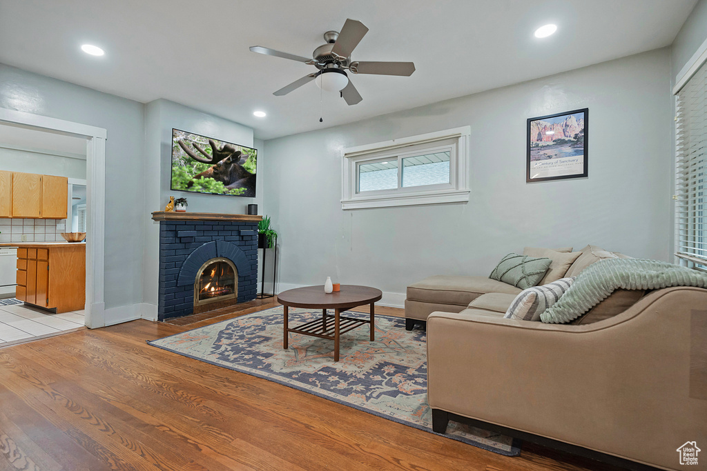 Living room with a fireplace, light hardwood / wood-style flooring, and ceiling fan