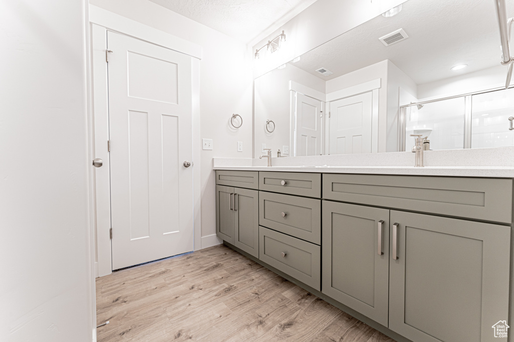 Bathroom with double vanity, wood finished floors, and a shower stall