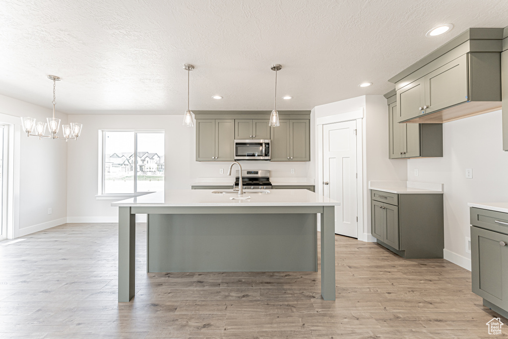 Kitchen with appliances with stainless steel finishes, gray cabinets, light countertops, baseboards, and a chandelier