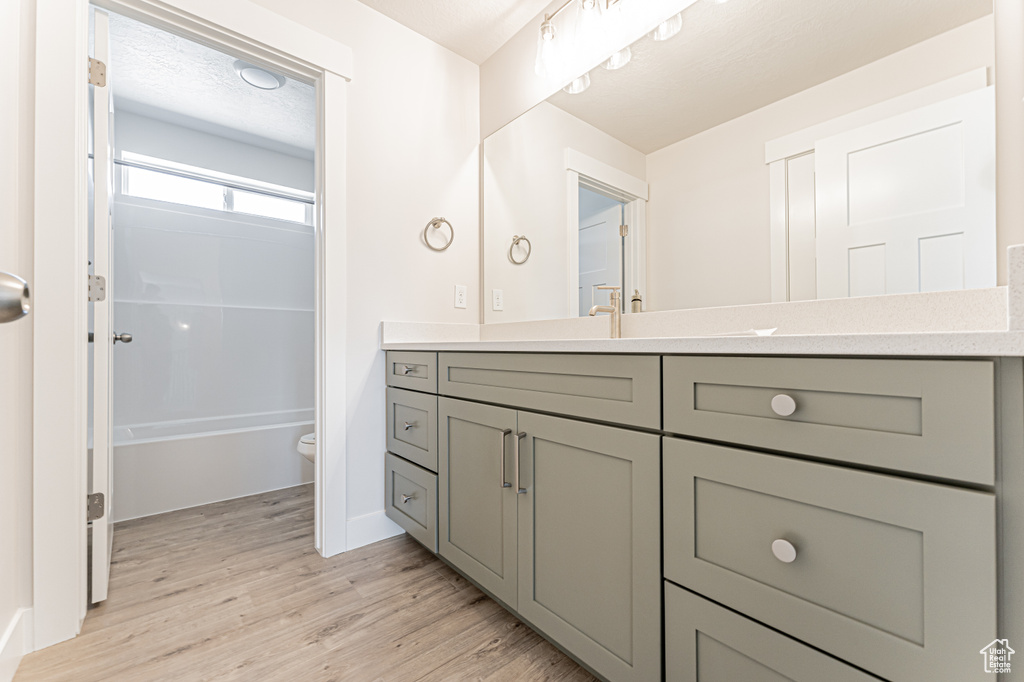 Full bath with vanity, toilet, wood finished floors, shower / bathtub combination, and baseboards