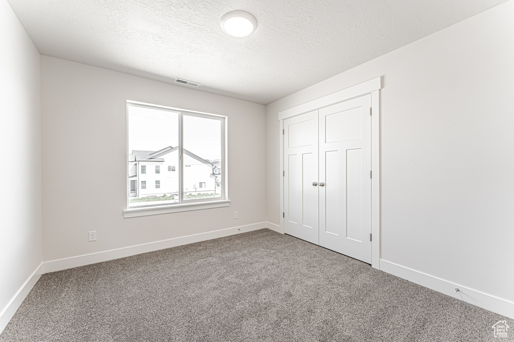 Unfurnished bedroom with carpet floors, baseboards, a textured ceiling, and a closet