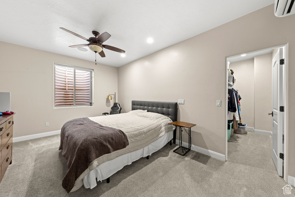 Bedroom with ceiling fan, a walk in closet, light carpet, and an AC wall unit